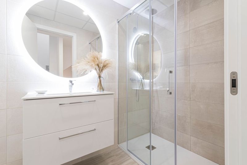 Bathroom in a holiday apartment with a large illuminated mirror and a shower stall.