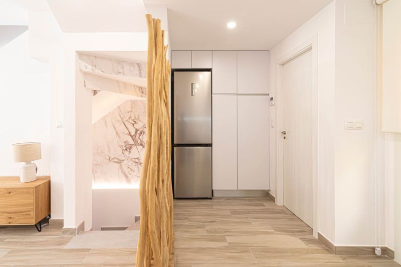 Interior of a holiday apartment with kitchen cabinets, refrigerator, and wooden decor flooring.