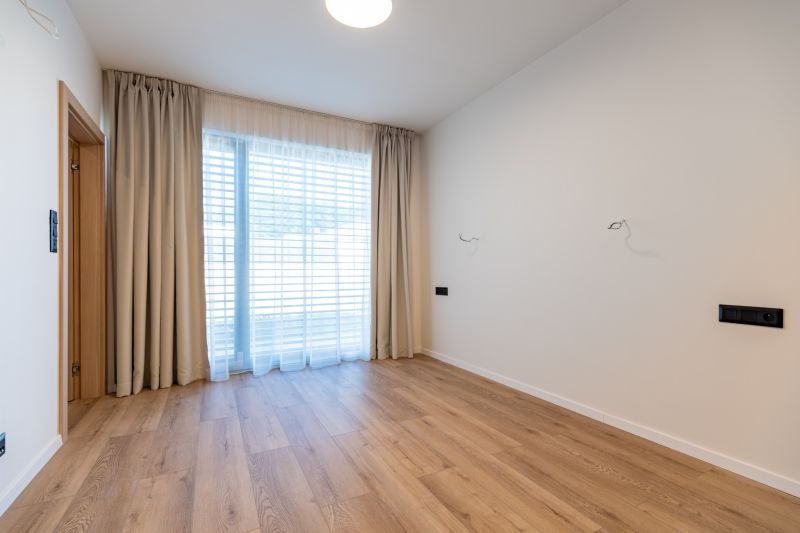 An empty room in a family house with wood-patterned flooring and a large window.