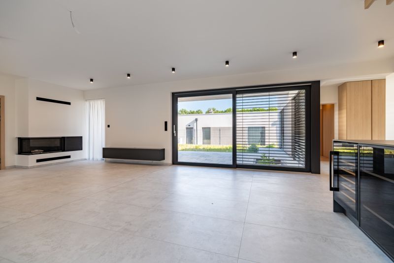 A spacious living room with a fireplace, large windows, and light flooring in a family house.