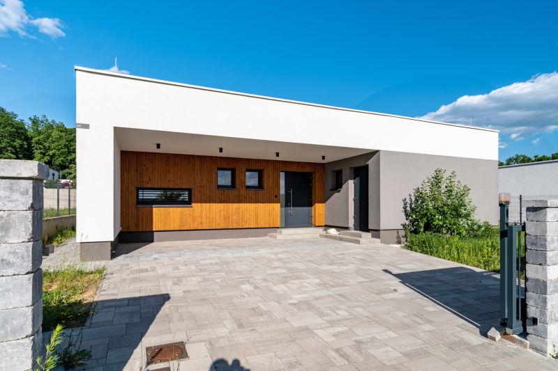 A family house in Košice-okolie with a minimalist facade, wooden elements, and a paved area.