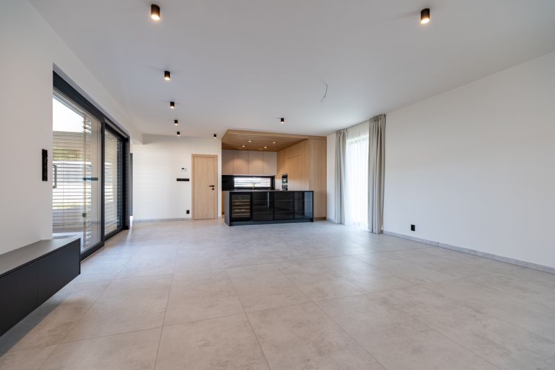 A minimalist interior of a family house with a kitchen, large windows, and light flooring.