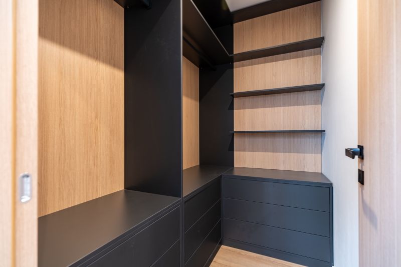 Corner built-in wardrobe with black drawers and wooden shelves in a family house.