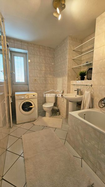 Bathroom of a 2-room apartment with a bathtub, sink, washing machine, and toilet.