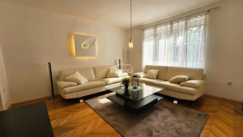 Living room in a 2-room apartment with a white couch and a wooden decor floor.