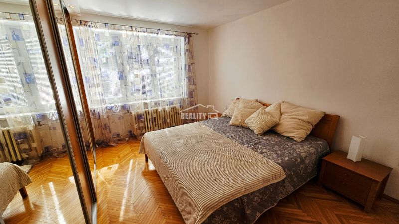 A bedroom in a two-room apartment with a wood-patterned floor and a large mirror.