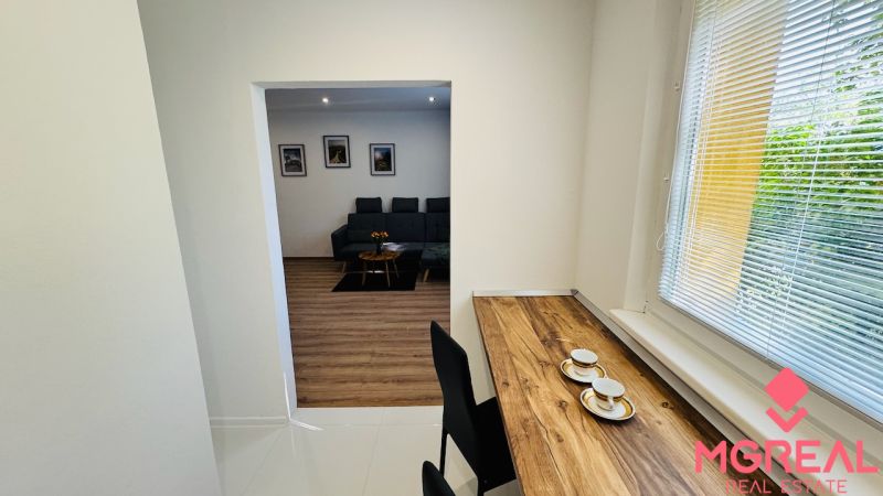 Interior of a 1-room apartment with a wooden decor floor, a sofa, and a table by the window.