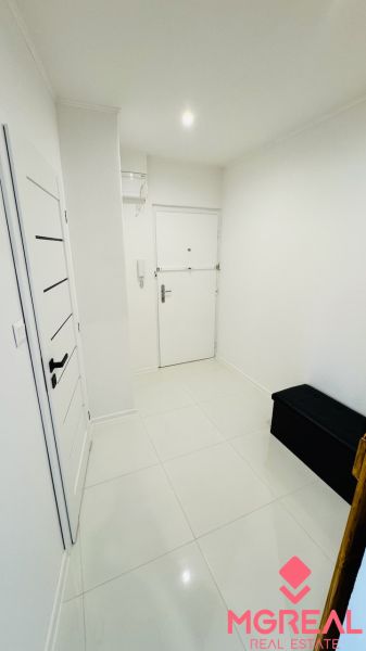 A white entrance hall with tiles and a dark bench in a studio apartment.