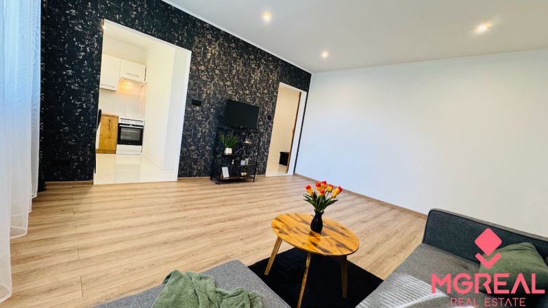 Living room of a one-room apartment with a wooden floor and flowers on the table.