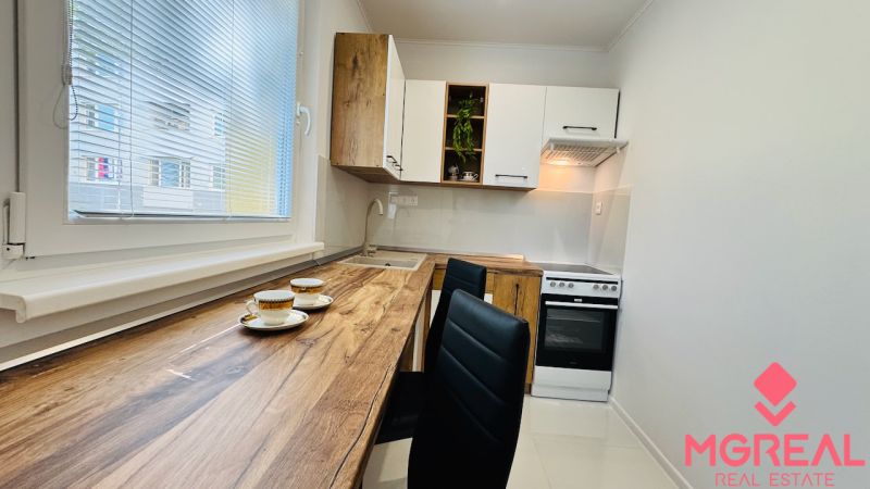 A kitchen in a studio apartment with wood-patterned flooring, white cabinets, and appliances.
