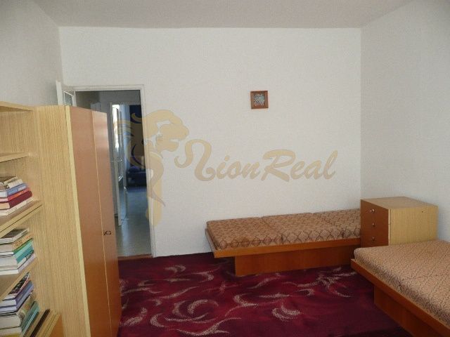 A room in a 2-room apartment with simple furniture and a red carpet.