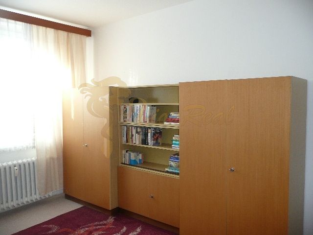 A room in a 2-room apartment with a bookshelf and a large wardrobe, floor with wooden decor.