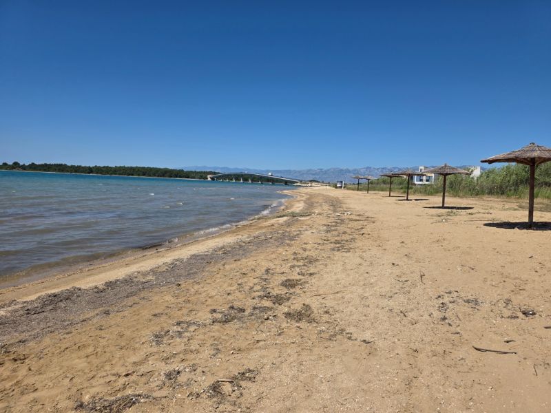 Sandy beach with reed umbrellas in Privlaka, with blue sky and sea.
