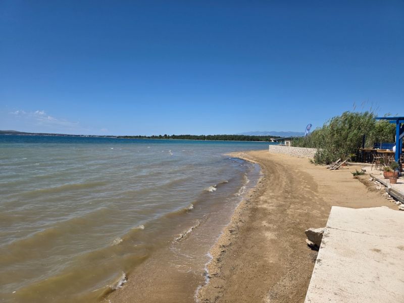 A sandy beach by the sea in Privlaka with a clear blue sky and water.