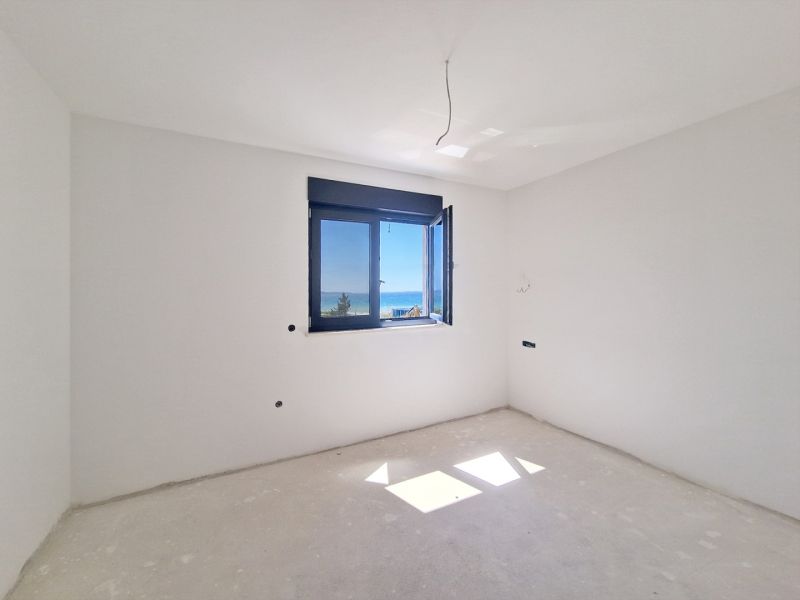 An empty room without furniture with a window and a sea view in a 3-room apartment.