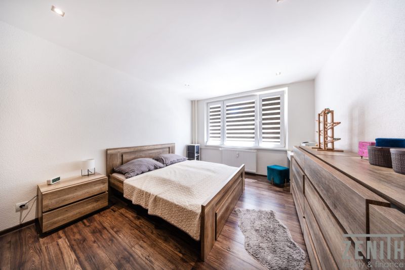 A bedroom in a 3-room apartment with a bed, a dresser, and a floor with a wooden decor.