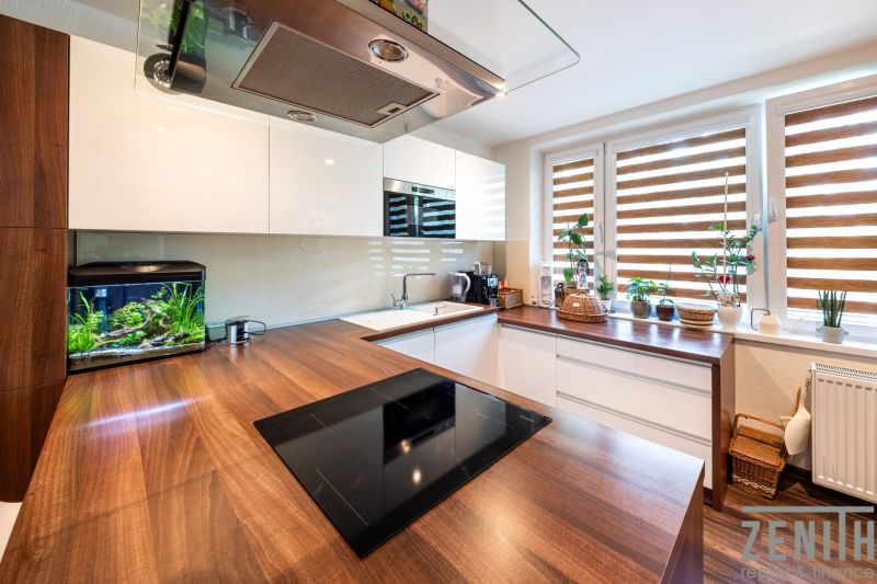 A kitchen in a 3-room apartment with a wooden decor floor and windows with plants.