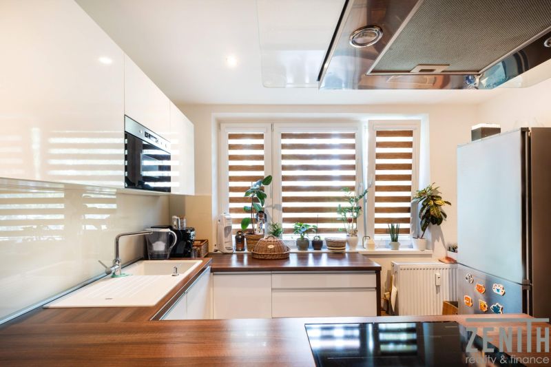 A kitchen in a 3-room apartment with plants on the windowsill and a floor with a wooden decor.