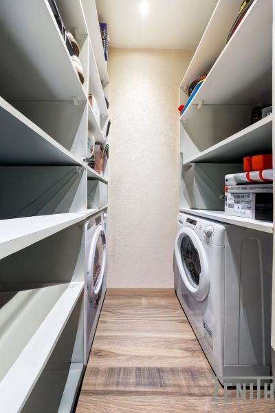 Storage space with shelves and a washing machine in a 3-room apartment with wood-patterned flooring.