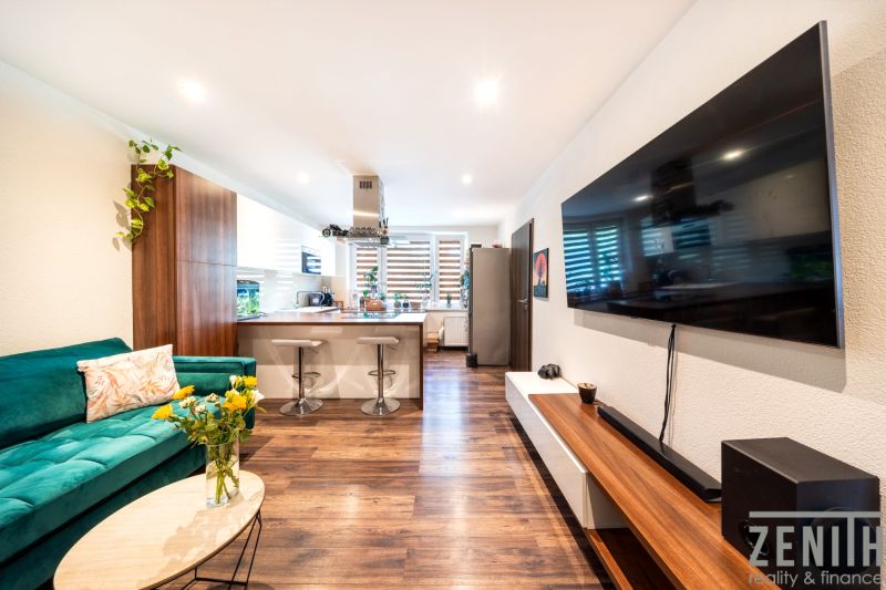 Living room in a 3-room apartment with a TV, sofa, and kitchen, floor with wood decor.