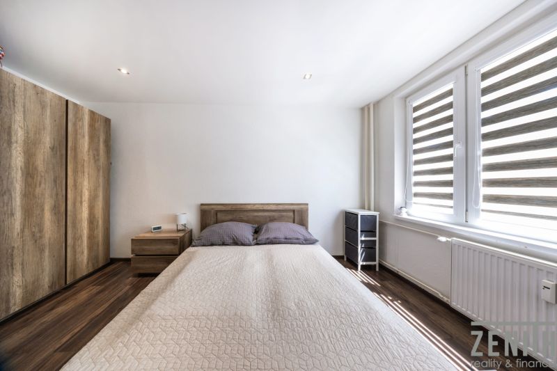 A bedroom with a bed, wood-patterned flooring, and large windows in a three-room apartment.