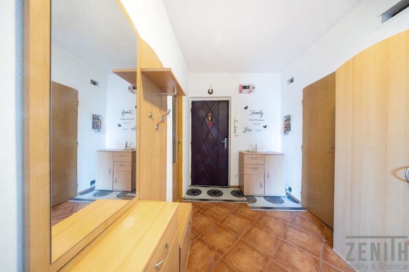 A hallway in a 3-room apartment with a wooden decor floor and a mirror.