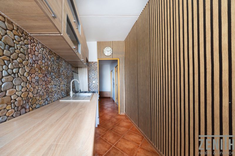 A kitchen with a wooden decor floor, stone tiles, and cabinets in a 3-room apartment.
