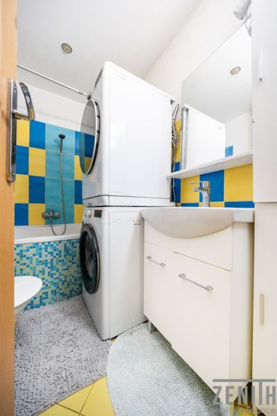 A bathroom in a 3-room apartment with a washing machine, dryer, and colorful tiles.