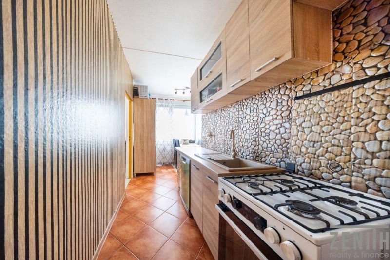 A kitchen in a 3-room apartment with a kitchen unit and tiles with a stone decor.