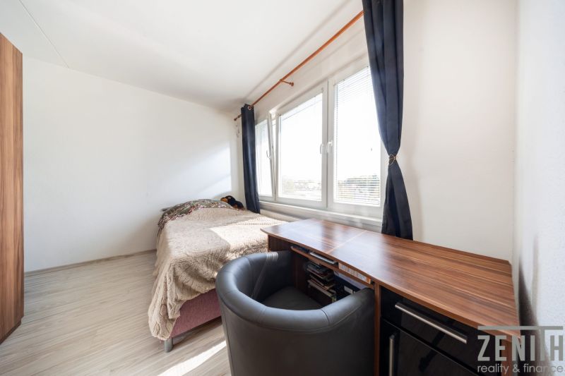 A room in a three-room apartment with a bed, a table, and windows with dark curtains.
