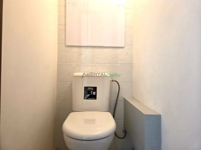 A toilet with tiled walls in a studio apartment.