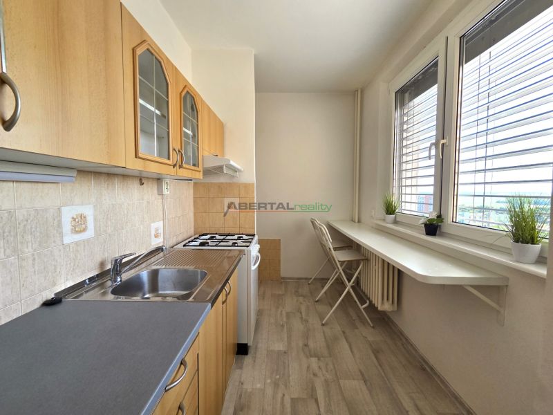 A kitchen in a one-room apartment with a wooden decor floor and white furniture.