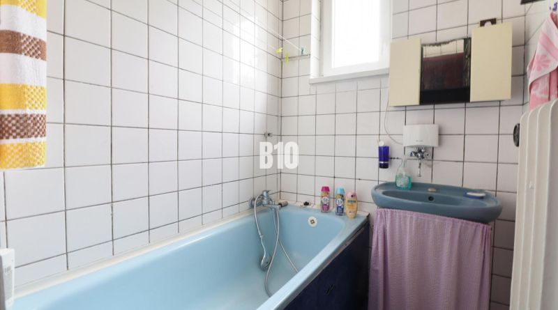 Bathroom with a bathtub and a sink in a family house. White tiles and a light blue bathtub.