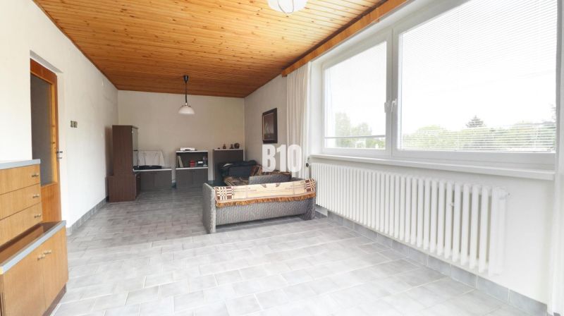 Living room interior with a wooden ceiling, sofa, large window, and light gray floor.