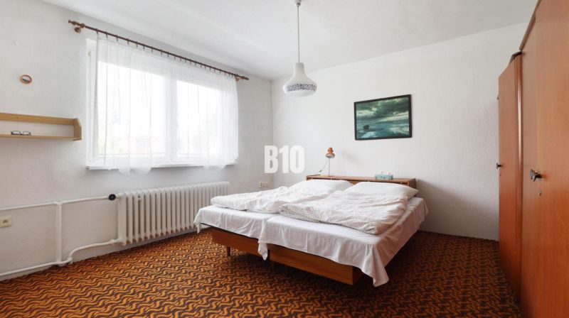 Bedroom in a family house with a bed, orange carpet, and a painting on the wall.