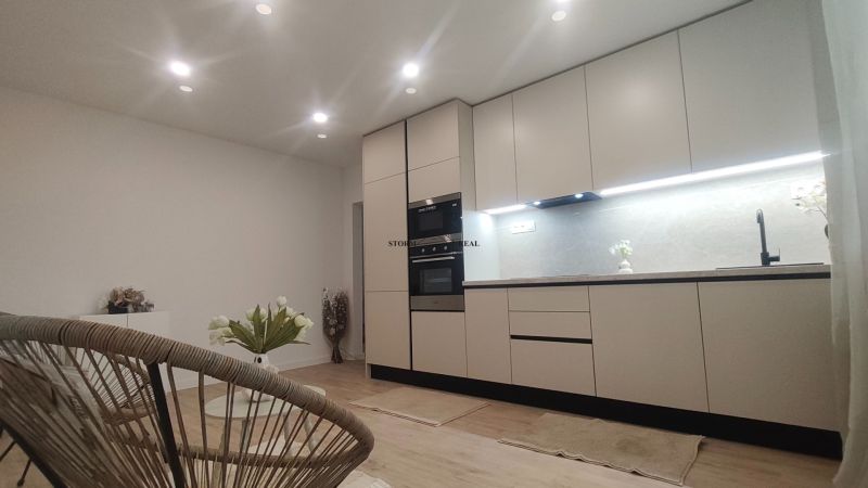 A kitchen in a 4-room apartment with a wooden decor floor, white cabinets, and plants.