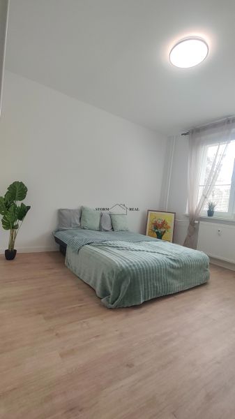 Bedroom in a 4-room apartment with a bed, a plant, and a wooden decor floor.