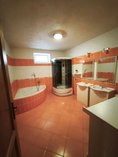 A bathroom in a family house with orange tiles, a bathtub, and a shower corner.