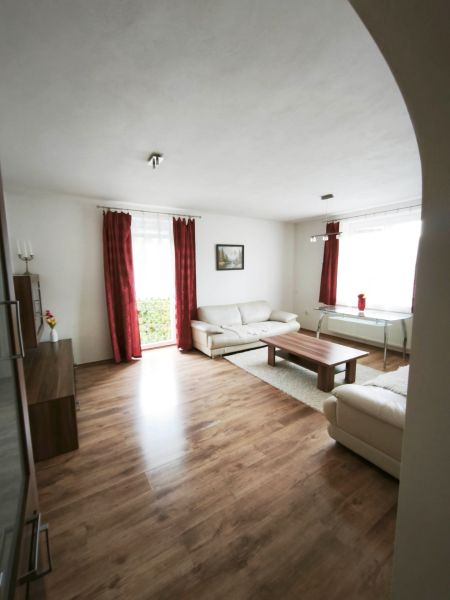 Living room of a family house with a wood-patterned floor, white furniture, and red curtains.