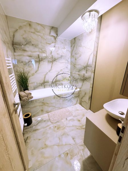 A bathroom with a bathtub, chandelier, and marble tiles in a 2-room apartment.