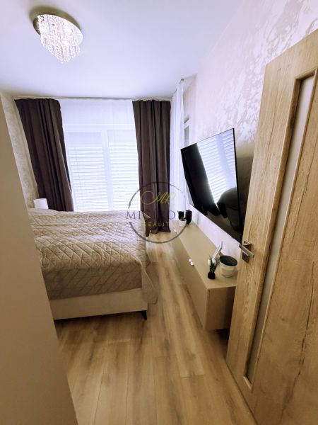 Bedroom in a 2-room apartment with wood-patterned flooring and a TV on the wall.