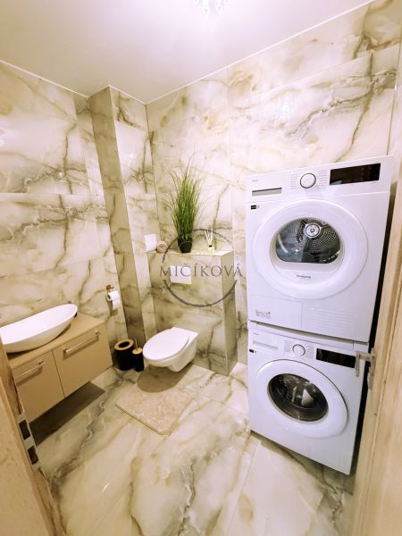 A bathroom with a washing machine and dryer in a 2-room apartment with marble tiles.