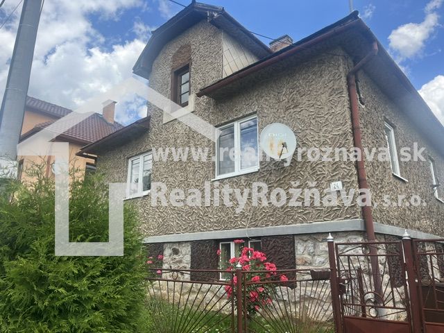 A family house in Rudná with a textured facade, a green fence, and flowers in the garden.