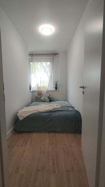 Narrow bedroom with a bed and a window, wooden decor flooring, bright interior.