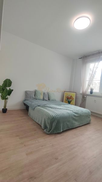 A bright room with a bed, a houseplant, and a wooden decor floor in a 4-room apartment.