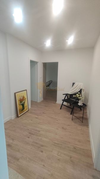 Interior of a 4-room apartment with a wooden decor floor, an armchair, and a painting.