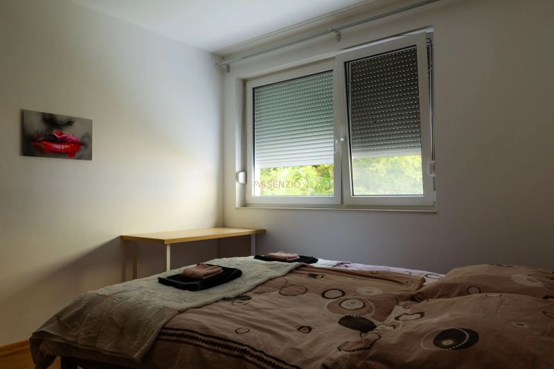 Bedroom in a two-room apartment with a window, table, and painting on the wall.