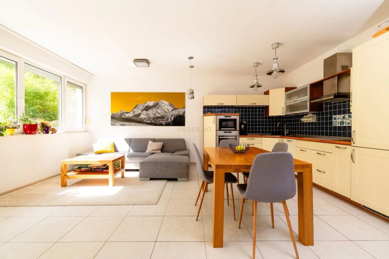 Living room with kitchen, light sofa, dining table, large windows, art on the wall.