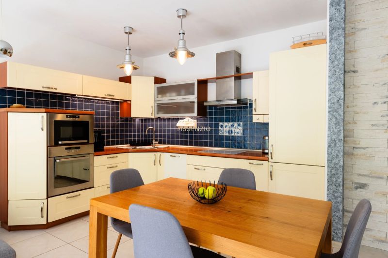 A kitchen in a 2-room apartment with a wooden table, blue tiles, and light cabinets.