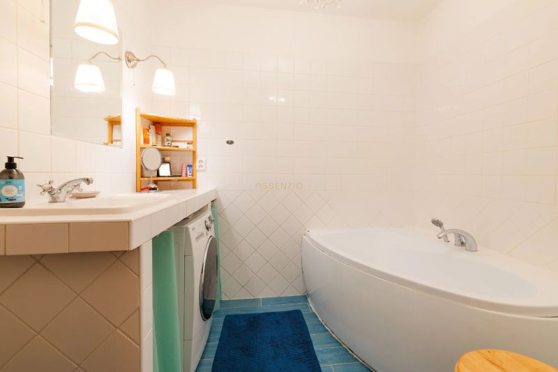 A bathroom with a bathtub, a washing machine, a blue rug, and white tiles in a 2-room apartment.